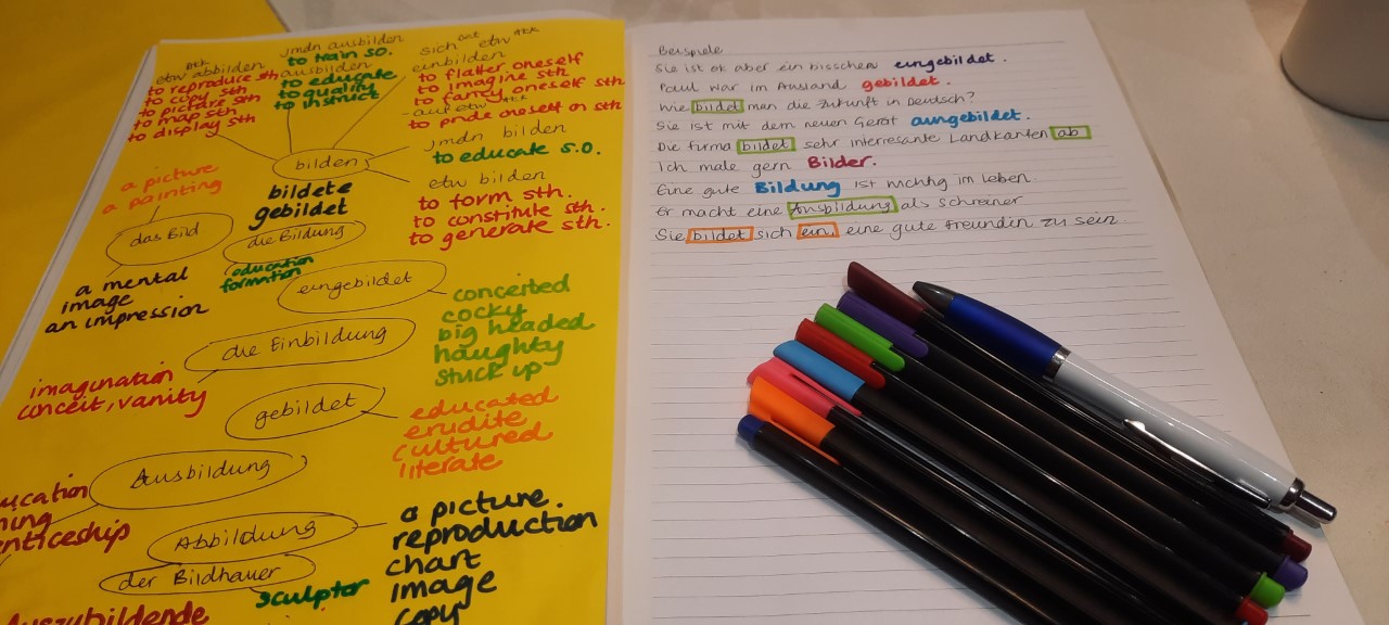A notebook open with coloured pens on one page. Lots of coloured writing on both pages.