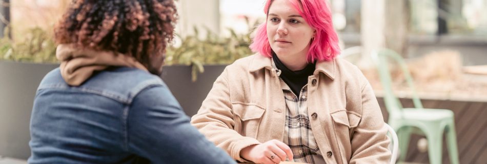 Two people outside sitting a a table and talking